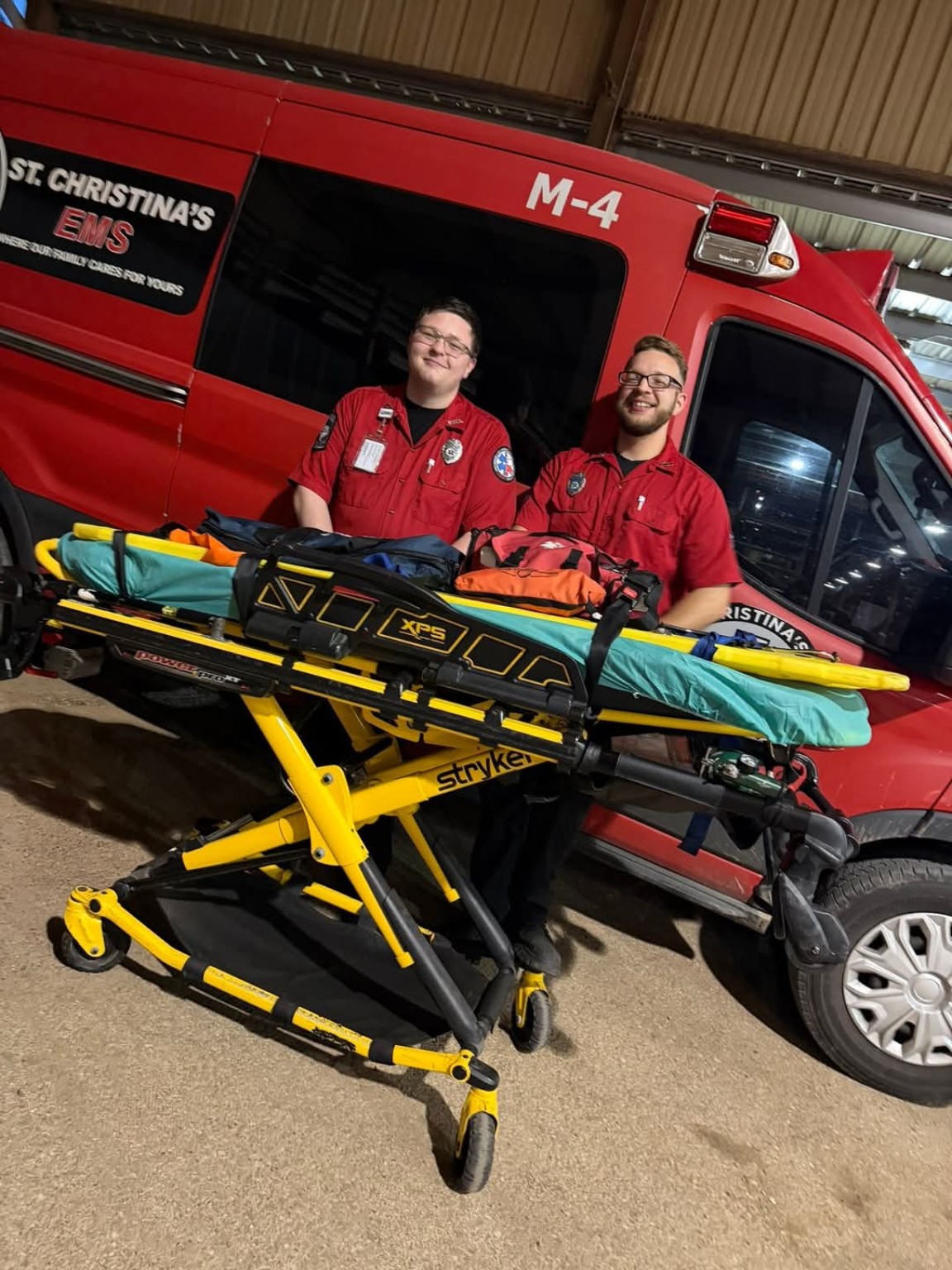 St. Christina’s EMS team members beside a stretcher and red ambulance